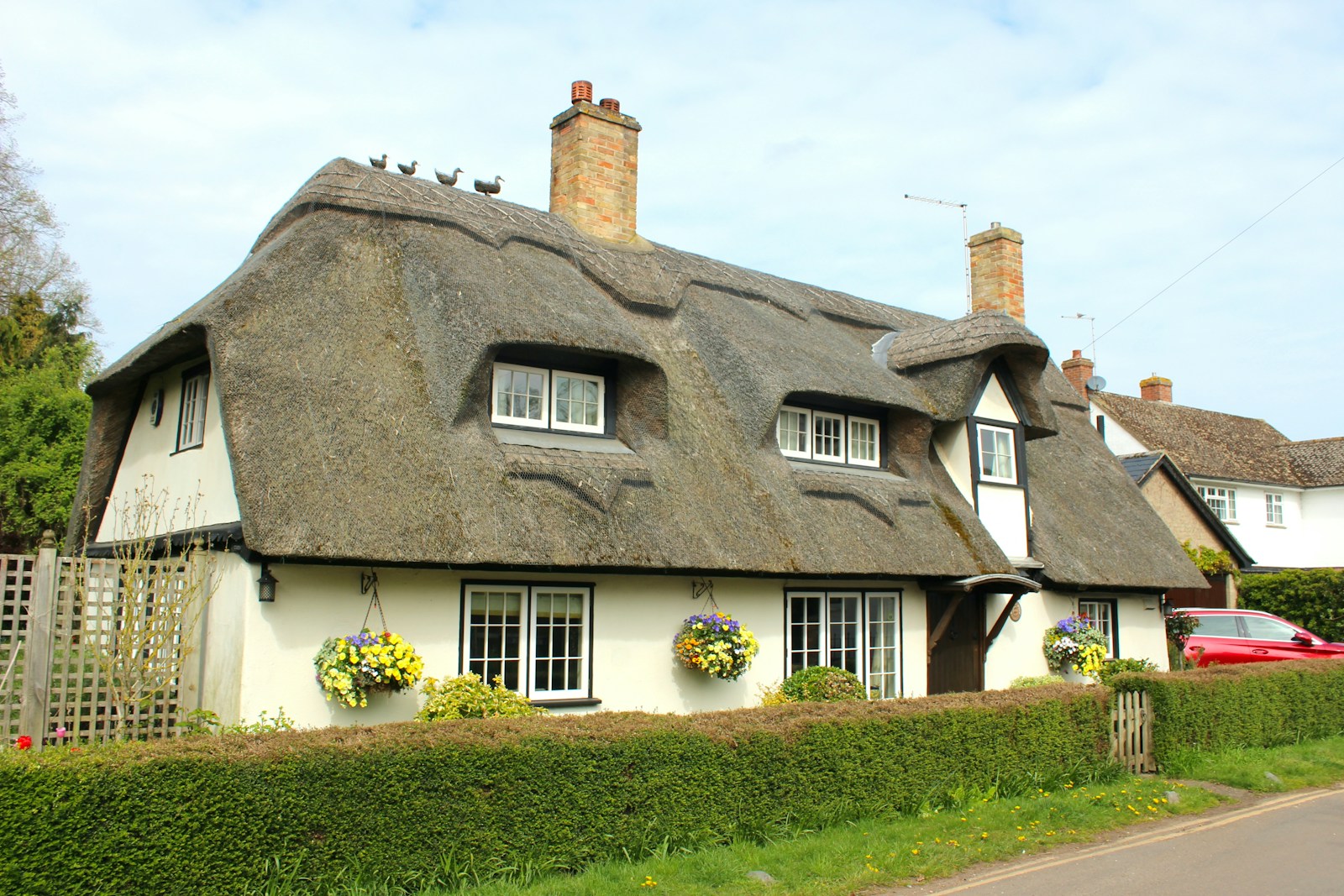 a white house with a thatched roof and a car parked in front of it